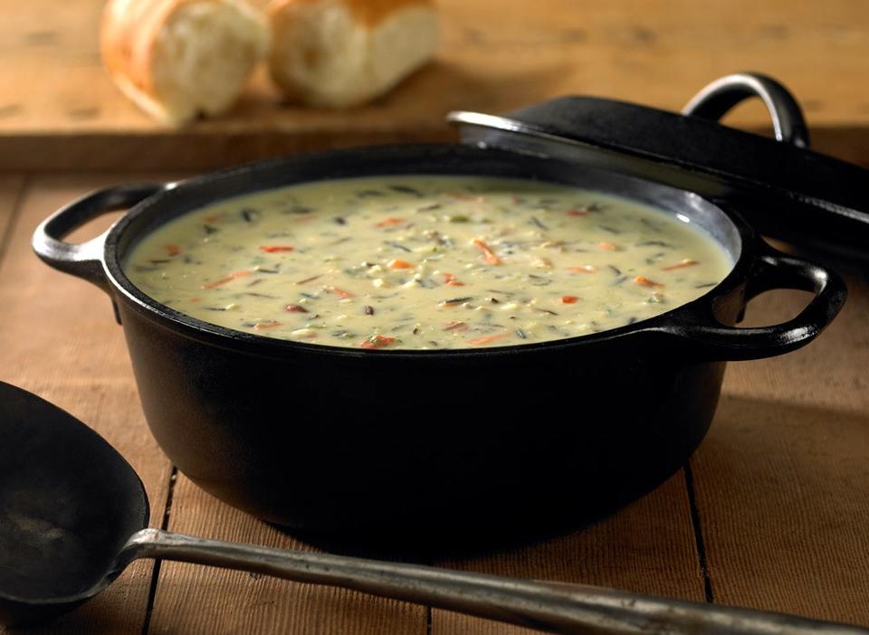 Wild rice soup in a cast iron pot on a wood table with bread and serving spoon.