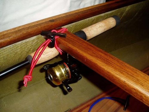 Red bungee holding a fishing pole to a wood frame.