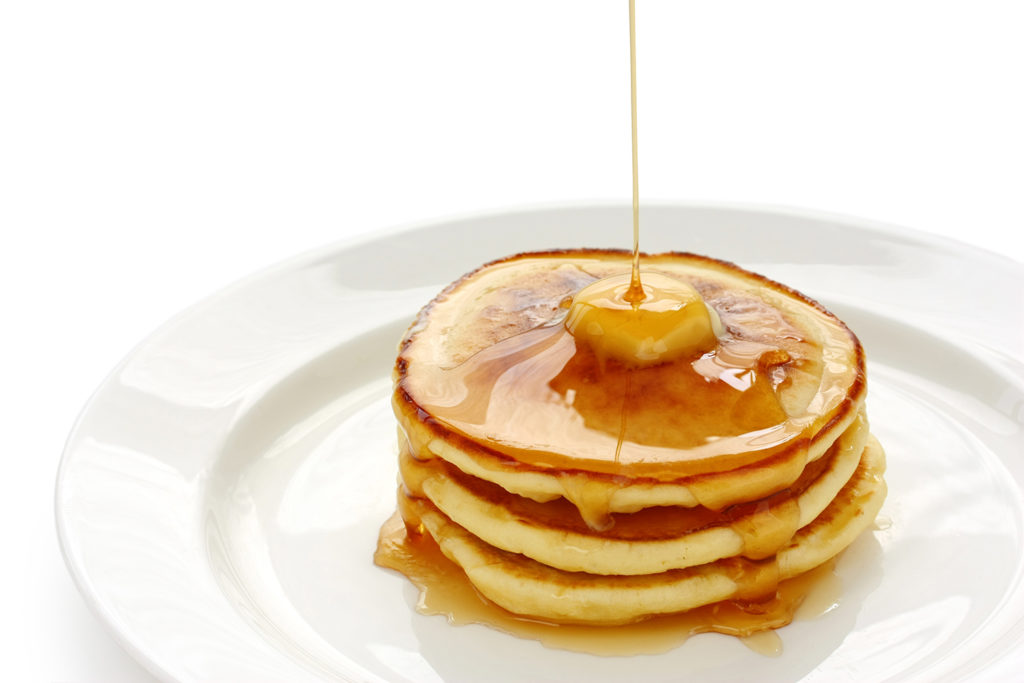 Pancake with butter and syrup being poured on top.