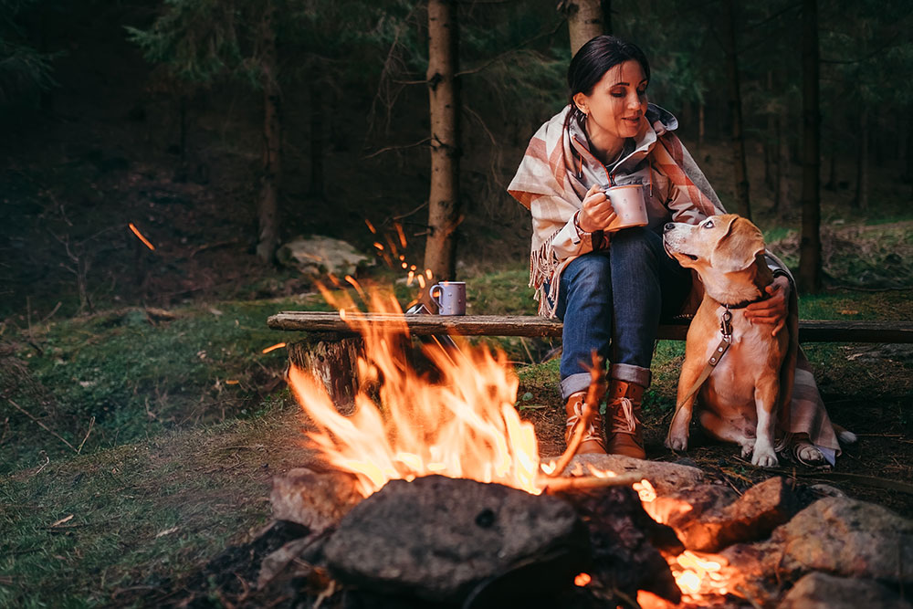 Woman sitting by a fire in the woods with her dog